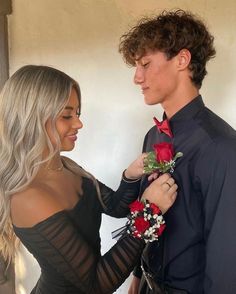 a man in a black shirt is holding a red rose while a woman in a black dress stands next to him