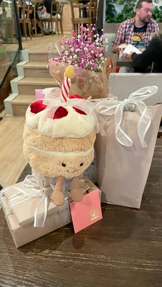 a stuffed animal sitting on top of a wooden table next to presents and flowers in a vase