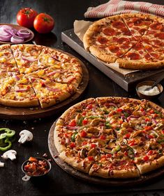 two pizzas with different toppings sitting on top of a table next to sliced onions and peppers