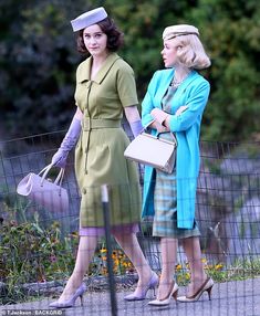 two women in dresses and hats are walking down the street with one holding a purse