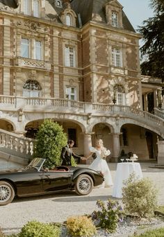 a bride and groom standing in front of an old fashioned car outside a large building