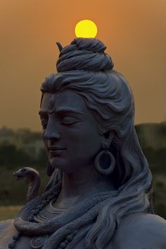 the sun is setting behind a statue of a woman with her head turned to look like a snake