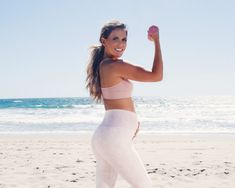 a woman is standing on the beach with her arm in the air and holding an apple