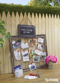 a wooden table topped with pictures and flowers next to a white picket fence covered in greenery