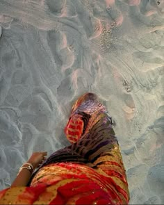 a woman's feet in the sand at the beach with her colorful sari