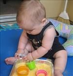 a baby sitting on top of a blue mat holding a plastic container filled with yellow liquid