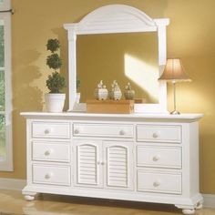 a white dresser with a mirror on top of it next to a lamp and potted plant