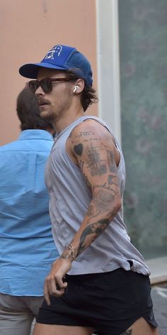 a man with tattoos on his arm is walking down the street in shorts and a cap