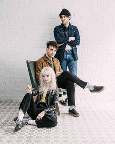 three people are sitting on the floor in front of a white brick wall and one person is holding her leg up