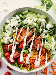 a salad with chicken, lettuce and tomatoes in a white bowl topped with dressing