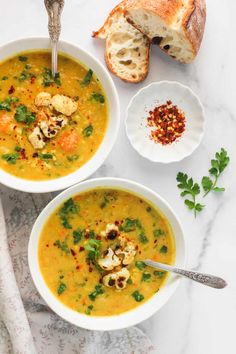 two bowls of soup with bread and garnish on the side, one bowl has cauliflower in it