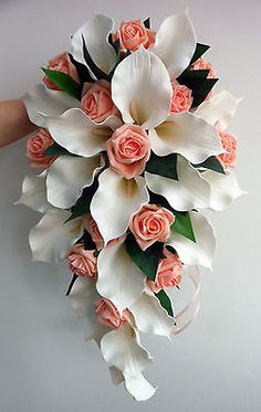 a bridal bouquet with pink roses and white calla lilies is held by someone's hand