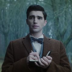 a man in a brown coat and bow tie holding a cell phone