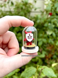 a hand is holding a small glass dome with a red and white figurine in it