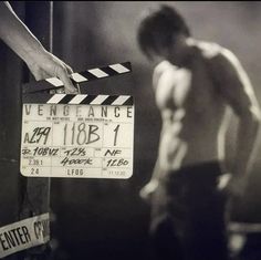 a shirtless man holding a movie clapper