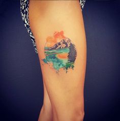 a woman's leg with a watercolor painting on it and mountains in the background