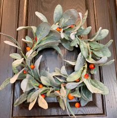 a wreath with orange berries and green leaves hanging on a wooden door frame in front of a brown door