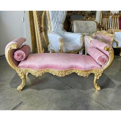 a pink and gold chaise lounge in front of a mirror with chairs behind it