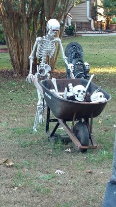 a skeleton sitting in a wheelbarrow filled with skulls and bones, next to a cemetery