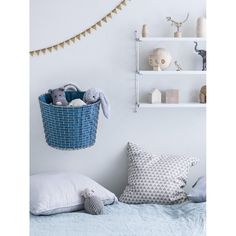 a blue basket filled with stuffed animals sitting on top of a bed next to pillows