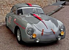 an old fashioned sports car is parked in front of a stone building with red ribbon on it