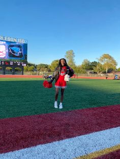 a girl in a cheerleader outfit stands on the field with her hands behind her back