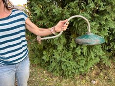 a woman holding a green lamp in front of a bush and shrub with her arm extended