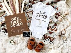 baby onesuit and other items laid out on a blanket next to a sign that says, our first rodeo