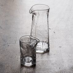 two glasses sitting on top of a table next to each other, one filled with water and the other empty