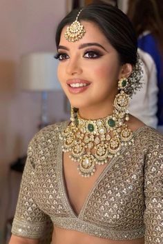 a woman in a gold and green outfit with jewelry on her neck, smiling at the camera