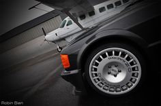 an airplane is parked next to a black car with white wheels and rims on it