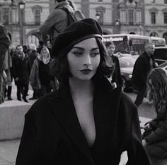 a woman walking down the street in a black dress and beret with her hands on her hips