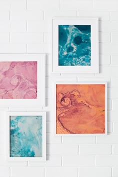 four different colored paintings hanging on a white brick wall