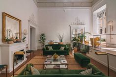 a living room filled with green couches next to a fire place under a mirror