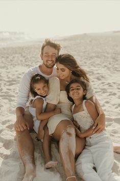 a man and two women sit on the sand with their children in front of them