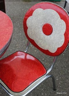 a red chair with a white flower on it sitting next to a table and chairs