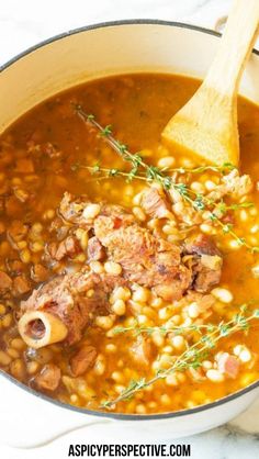 a pot filled with beans and meat next to a wooden spoon