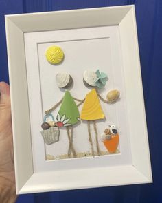 a person holding up a framed artwork with shells and other things in it's hands