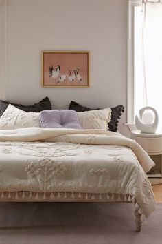 a bed with white sheets and pillows in a bedroom next to a painting on the wall