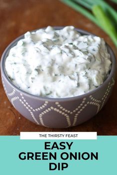 a bowl filled with green onion dip on top of a wooden table