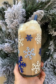 someone holding up a frosted drink in front of a christmas tree with blue and white snowflakes on it