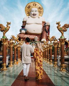 a man and woman standing in front of a giant buddha statue at the entrance to a temple