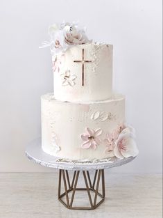 a three tiered cake with flowers on the side and a cross at the top