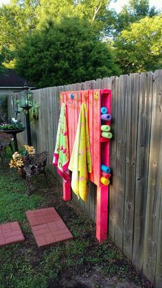 colorful towels hanging on the side of a wooden fence next to a potted plant