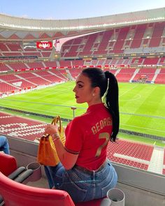 a woman sitting in the stands at a soccer stadium holding a purse and looking off into the distance