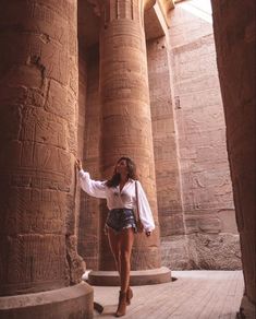 a woman standing in front of an ancient building with her hand up to the ceiling