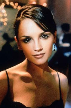 a close up of a person wearing a black dress and posing for a photo with lights in the background