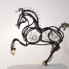 a sculpture of a horse with bells on it's hind legs and tail is shown in front of a white wall