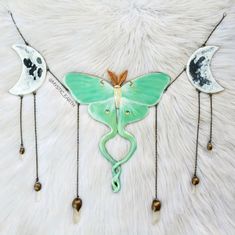 three butterflies with chains attached to them on a white fur covered surface, one is green and the other is brown