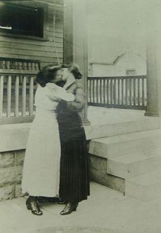 an old black and white photo of two women hugging on the front steps of a house